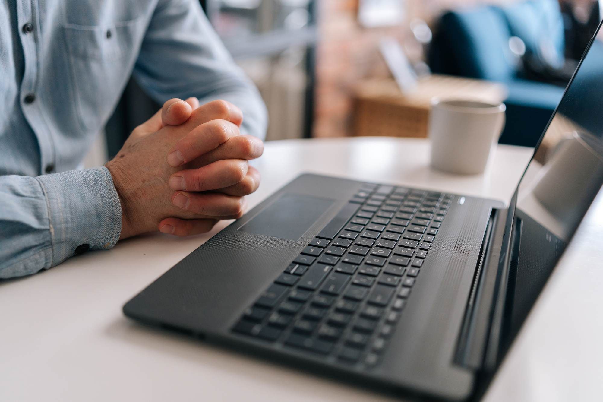 Meridian at Wylie Person with hands clasped sits at a table with an open laptop and a coffee cup in the background.