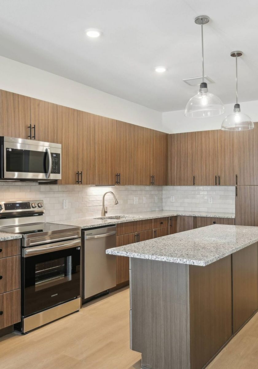 Meridian at Wylie Modern kitchen with wood cabinets, stainless steel appliances, island, and pendant lights.