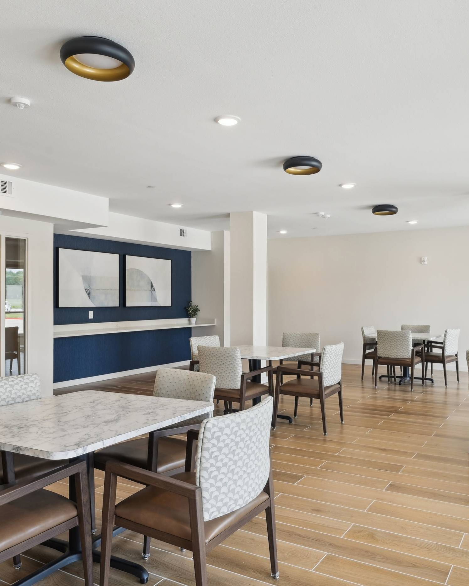 Meridian at Wylie Modern dining area with marble tables, patterned chairs, wooden floor, and abstract wall art.