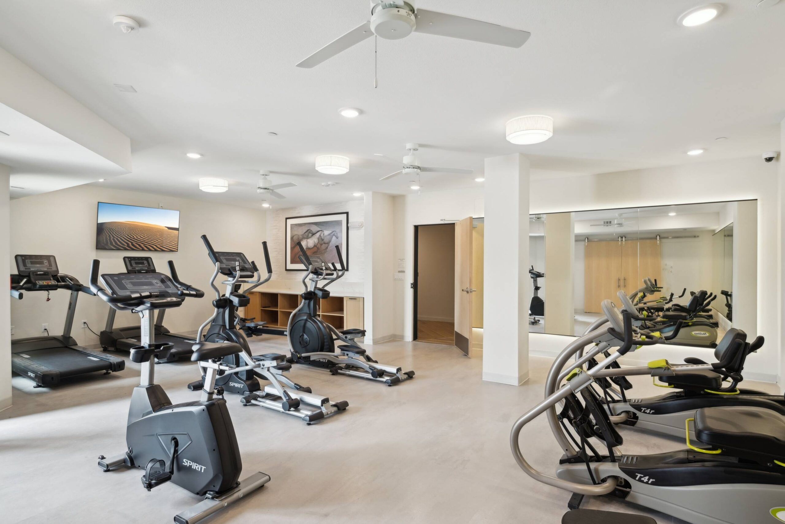 Meridian at Wylie Modern gym room with treadmills, ellipticals, stationary bikes, wall mirrors, and mounted TVs.