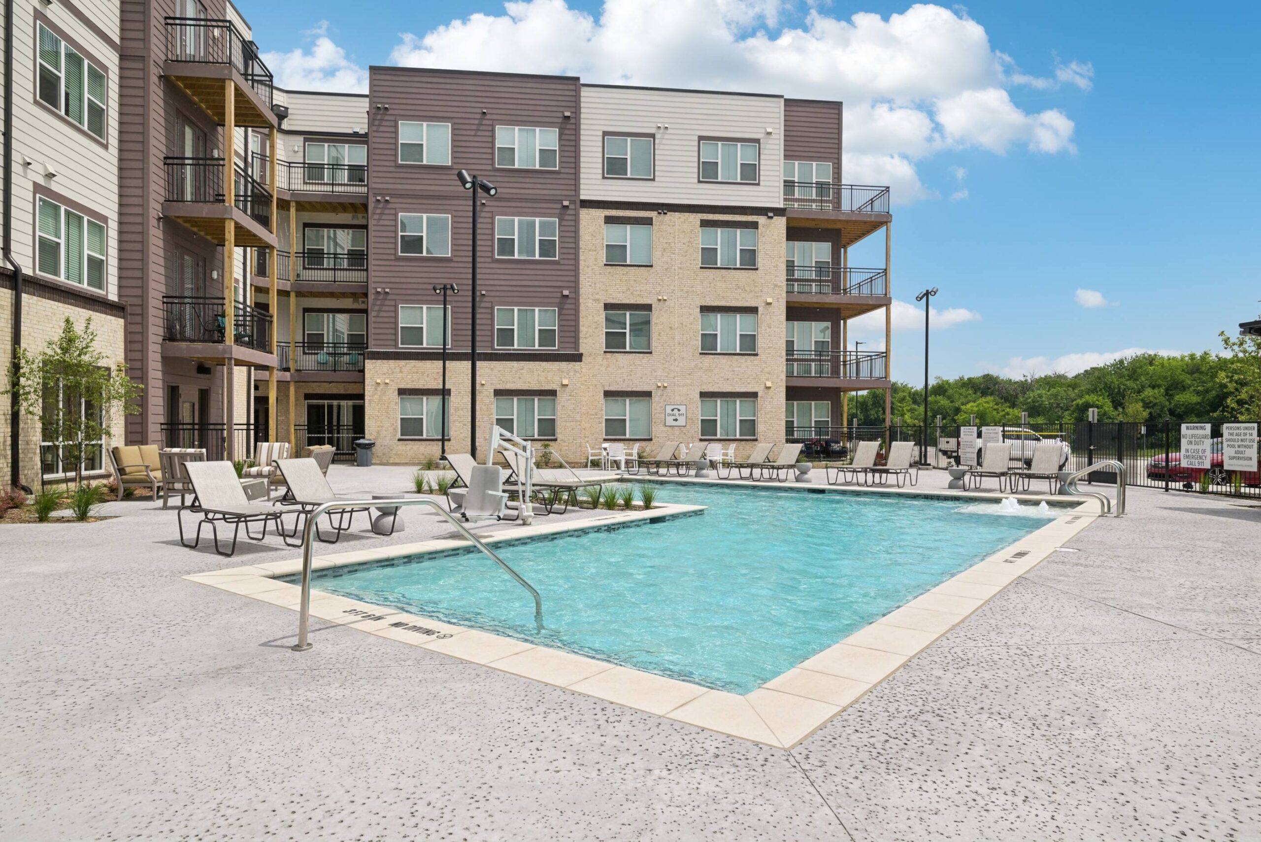 Meridian at Wylie Outdoor swimming pool with lounge chairs, surrounded by a modern apartment building under a blue sky.