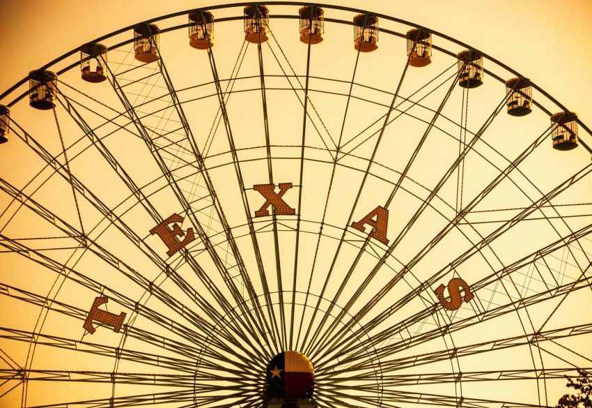 Meridian at Wylie Close-up of a Ferris wheel with "TEXAS" spelled out on it, against an orange sky background.