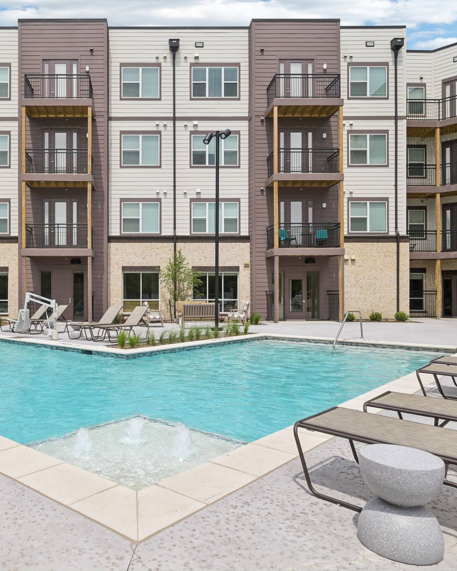 Meridian at Wylie Modern apartment building with balconies overlooks a swimming pool and lounge chairs on a sunny day.
