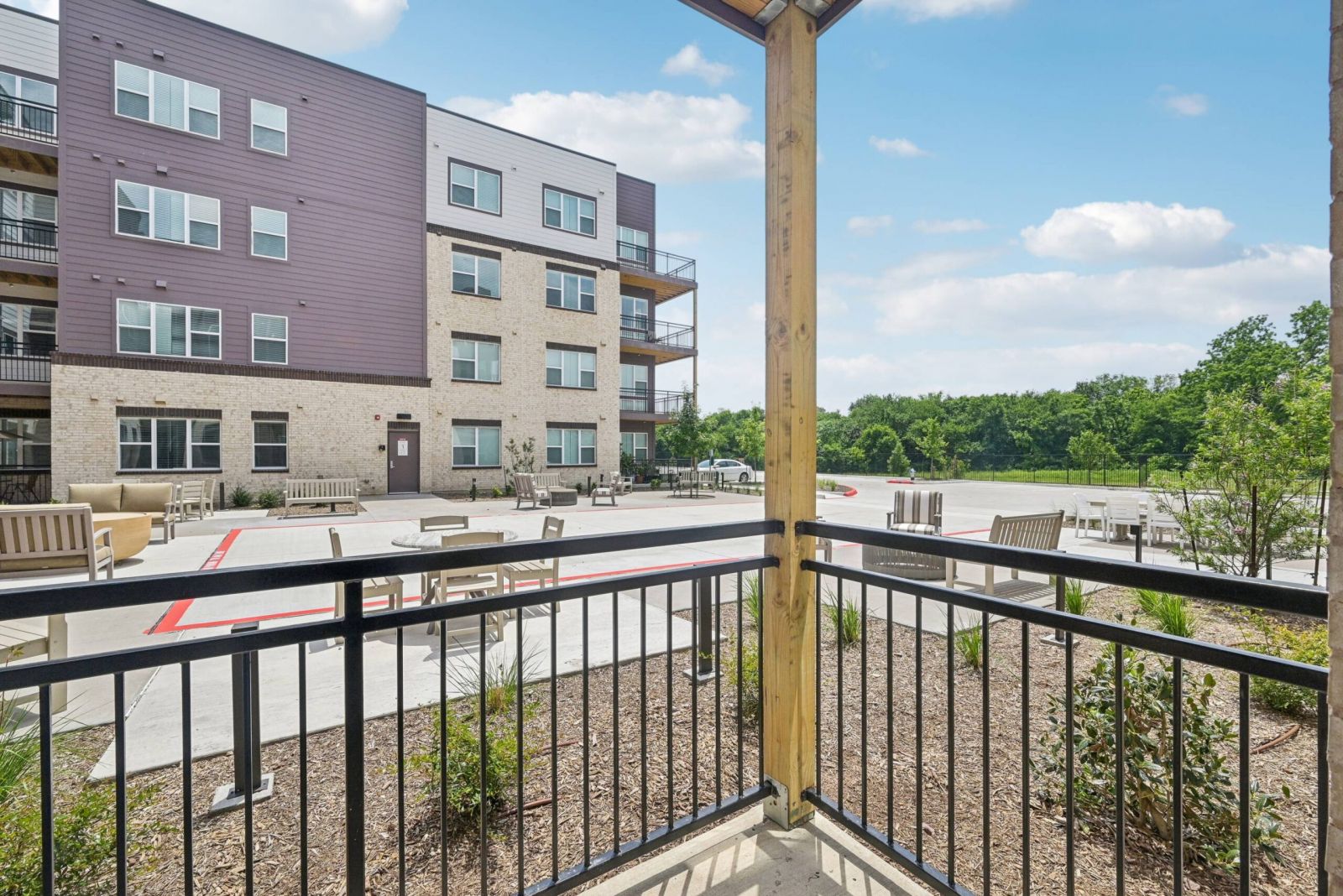Meridian at Wylie View from a balcony overlooking a modern apartment building and outdoor seating area on a sunny day.